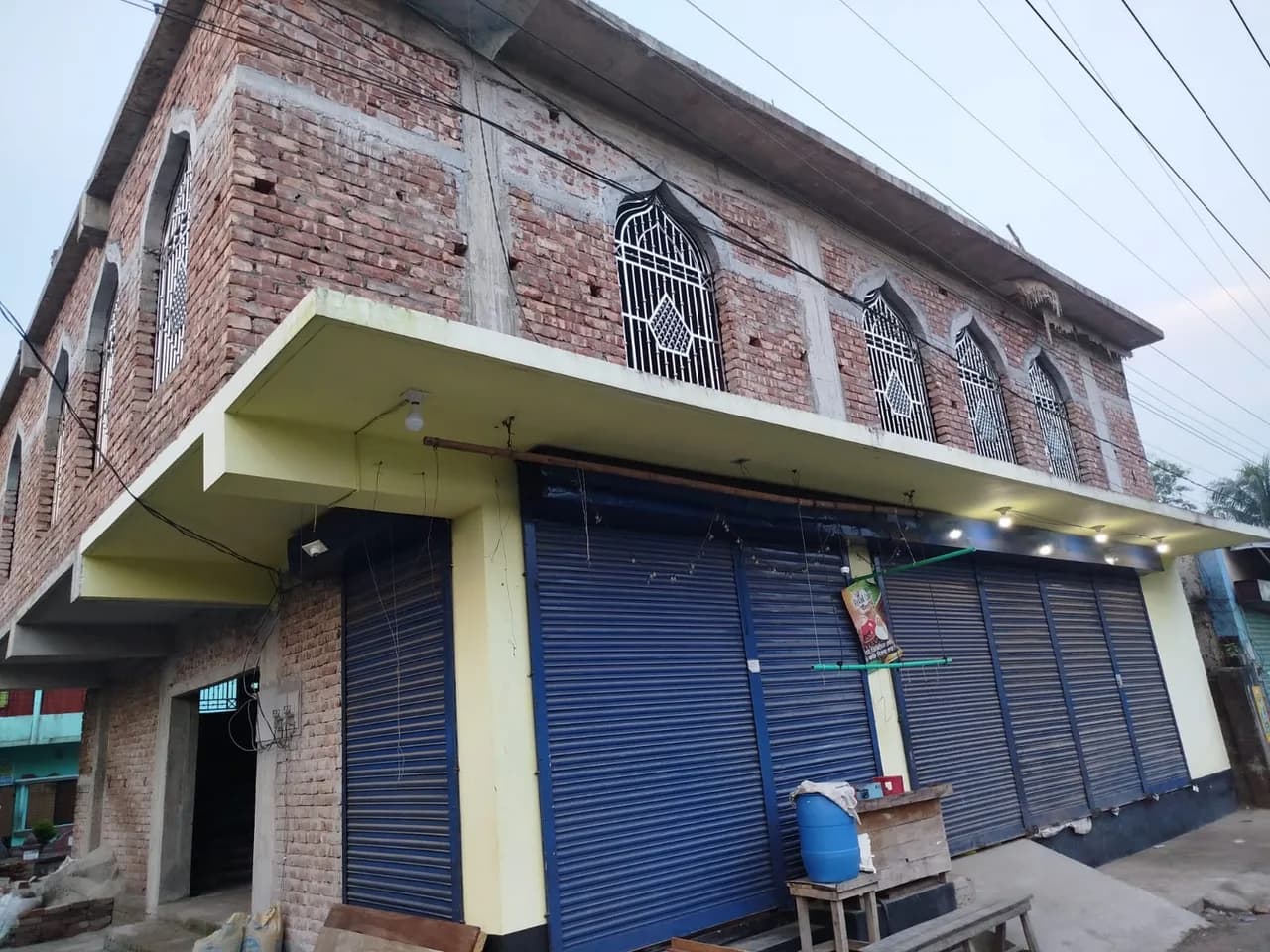 ফ্যাকাশে হলুদ নিচতলা, নীল শাটার ও উপরতলার খিলানযুক্ত জানালাসহ রাস্তার দৃশ্য